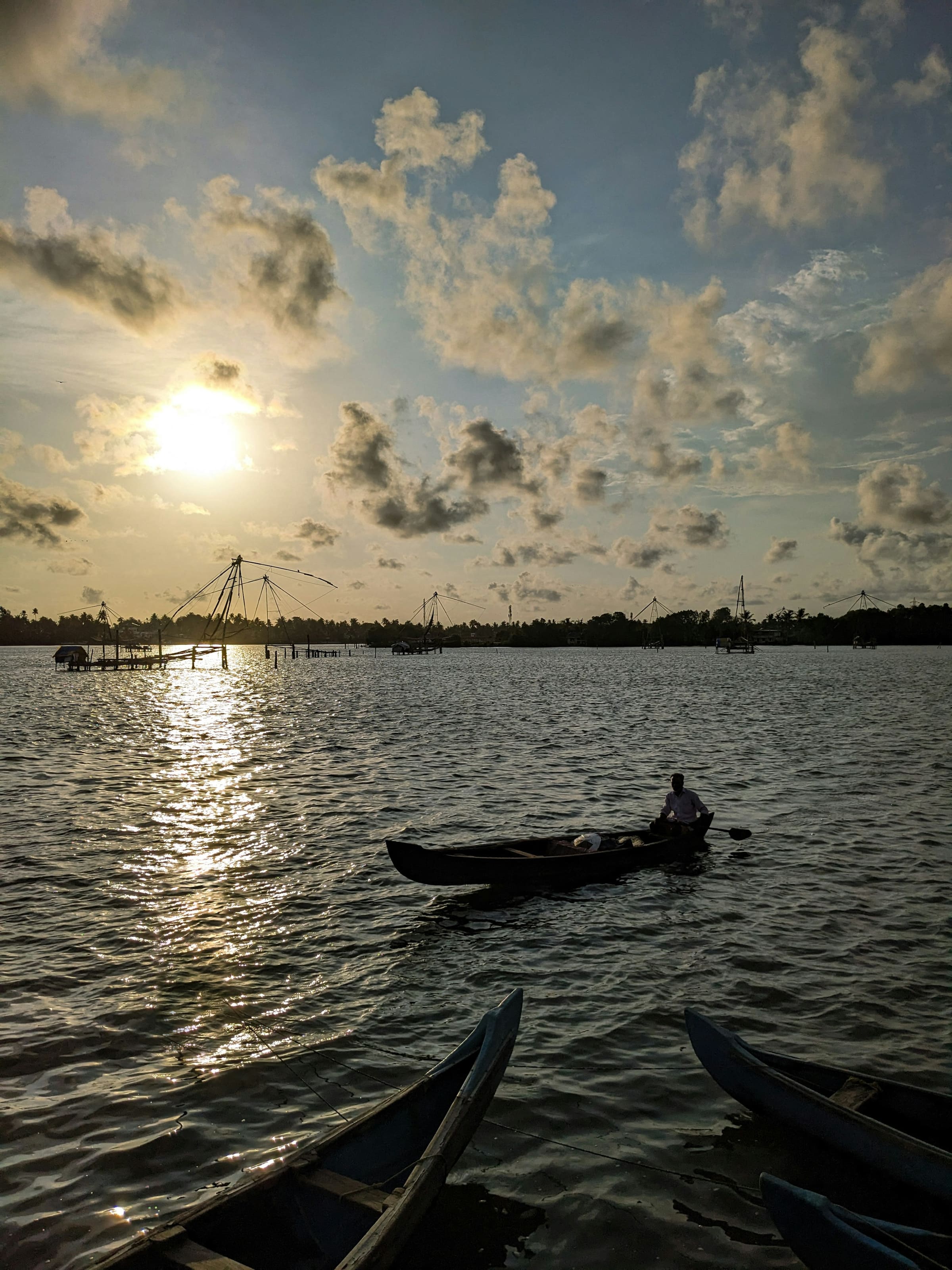 Cantilevered fishing nets silhouetted on the Kochi waterfront under a late afternoon sun.